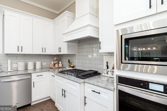 kitchen featuring white cabinets, custom range hood, appliances with stainless steel finishes, light stone counters, and tasteful backsplash