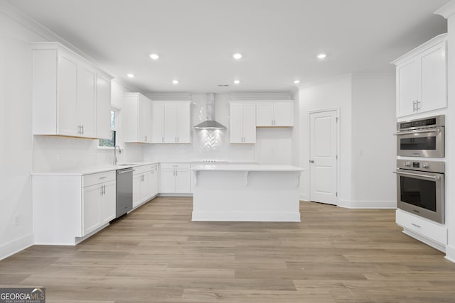 kitchen featuring sink, appliances with stainless steel finishes, white cabinetry, a center island, and wall chimney exhaust hood