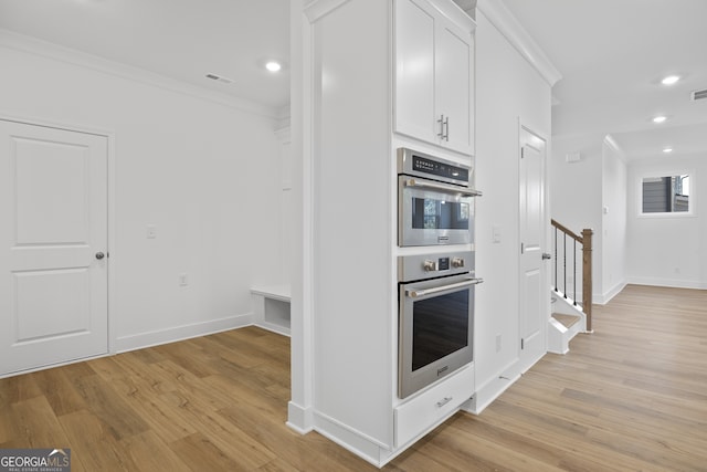 kitchen with white cabinetry, stainless steel double oven, crown molding, and light hardwood / wood-style flooring