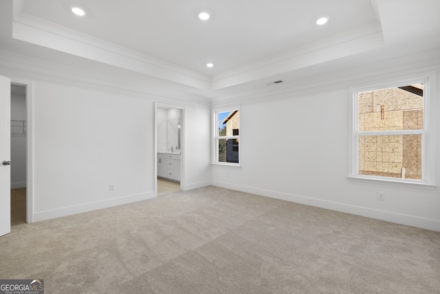 unfurnished bedroom featuring connected bathroom, crown molding, a walk in closet, light carpet, and a tray ceiling