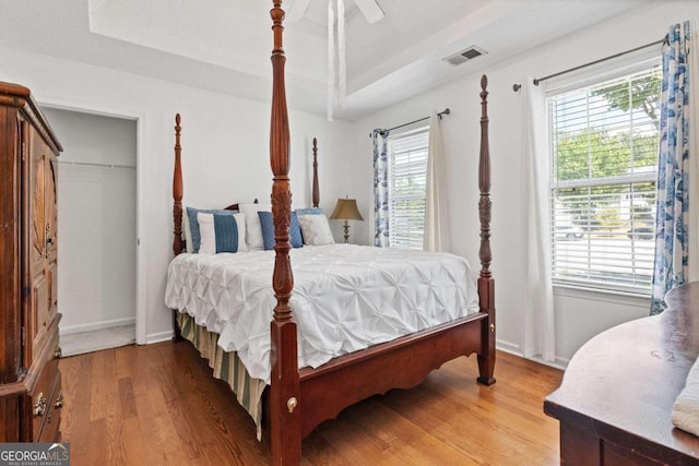 bedroom featuring a tray ceiling, multiple windows, light hardwood / wood-style flooring, and ceiling fan