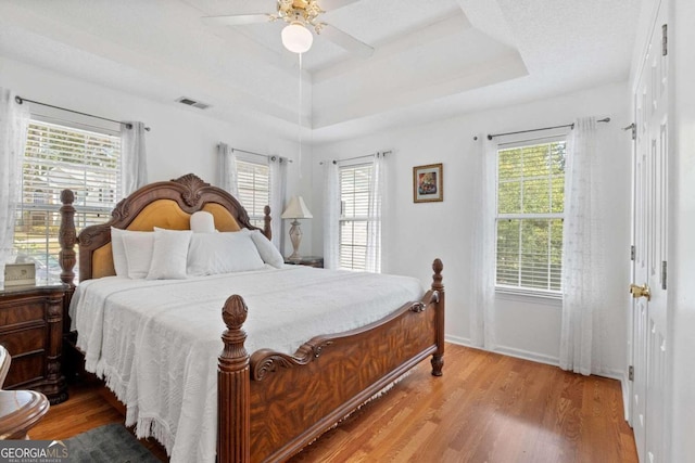 bedroom with a tray ceiling, multiple windows, hardwood / wood-style flooring, and ceiling fan