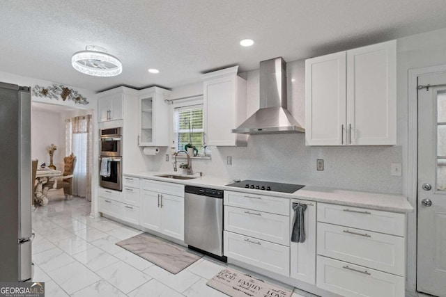 kitchen with white cabinetry, stainless steel appliances, sink, and wall chimney range hood