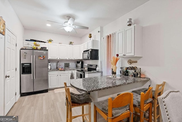 kitchen featuring dark stone countertops, stainless steel appliances, ceiling fan, a breakfast bar area, and light hardwood / wood-style floors