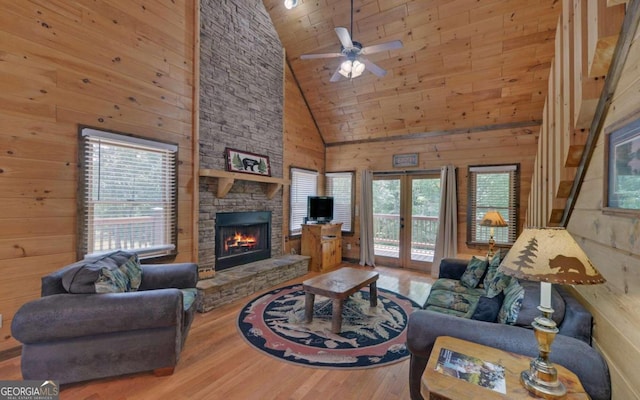 living room with ceiling fan, wood walls, high vaulted ceiling, and a fireplace