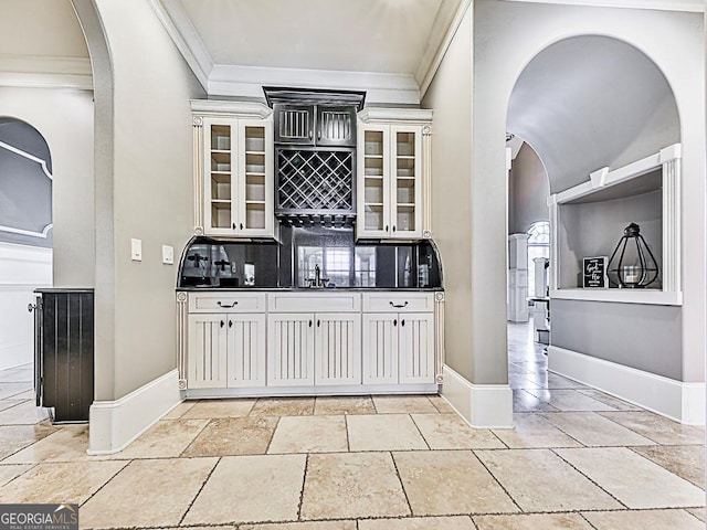 indoor bar with crown molding, arched walkways, decorative backsplash, baseboards, and stone tile floors