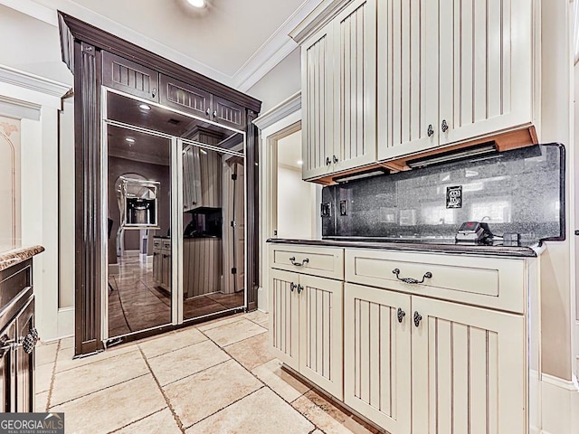 kitchen featuring dark stone countertops, light tile patterned floors, cream cabinets, crown molding, and tasteful backsplash