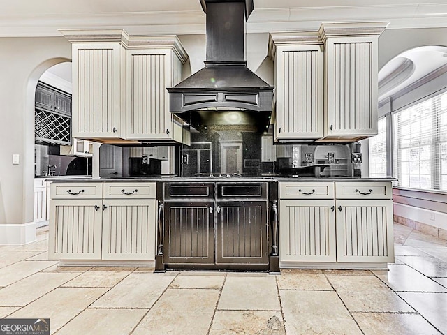 kitchen featuring crown molding, wall chimney exhaust hood, dark countertops, tasteful backsplash, and baseboards