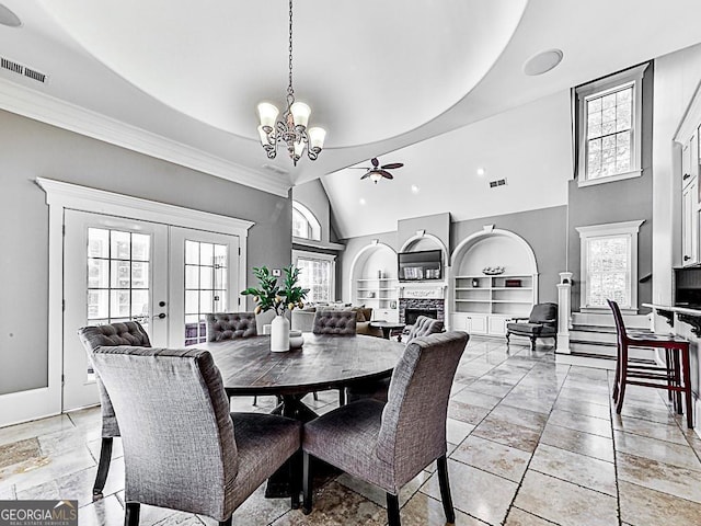 dining room featuring a stone fireplace, a healthy amount of sunlight, ceiling fan with notable chandelier, and french doors