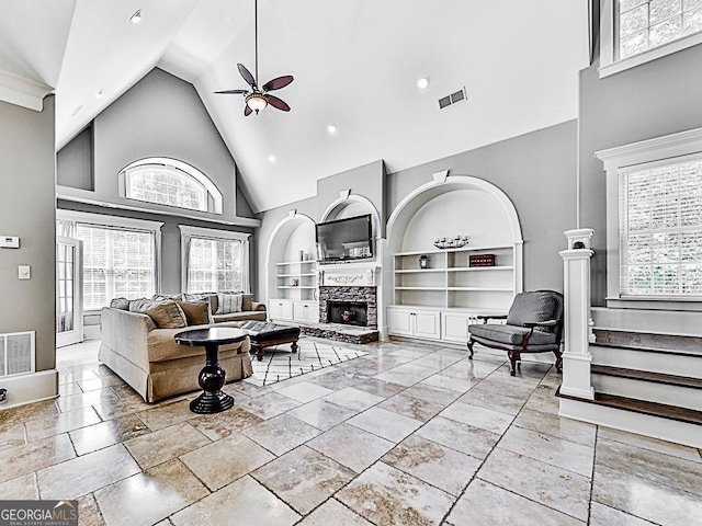 living room with high vaulted ceiling, ceiling fan, built in shelves, plenty of natural light, and a fireplace with raised hearth