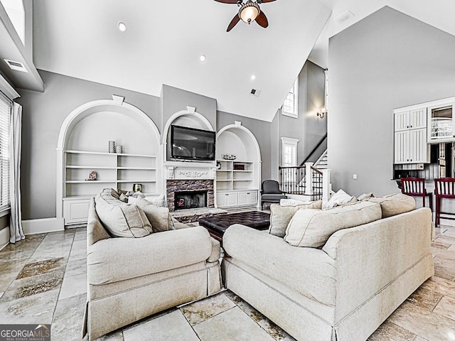 living room with built in features, high vaulted ceiling, a fireplace, and ceiling fan