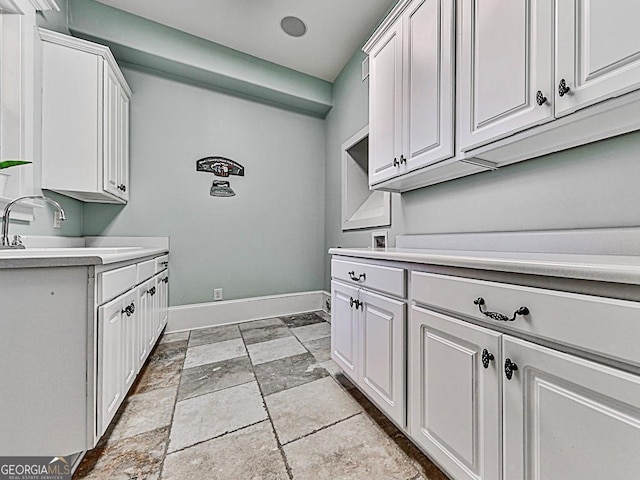 clothes washing area featuring a sink, baseboards, and light stone finish flooring