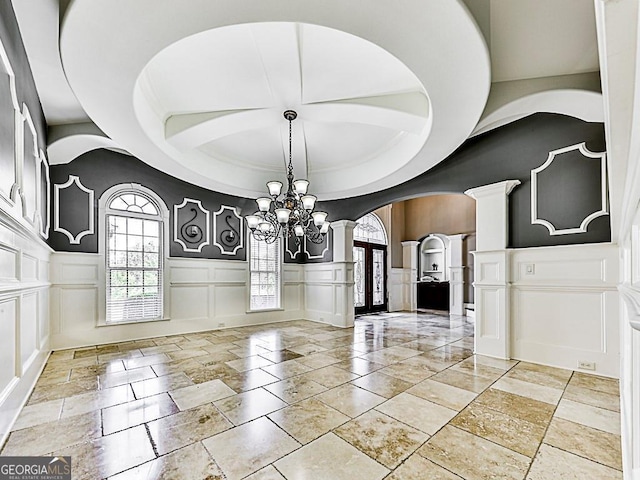 entryway with a decorative wall, ornate columns, a chandelier, plenty of natural light, and a wainscoted wall