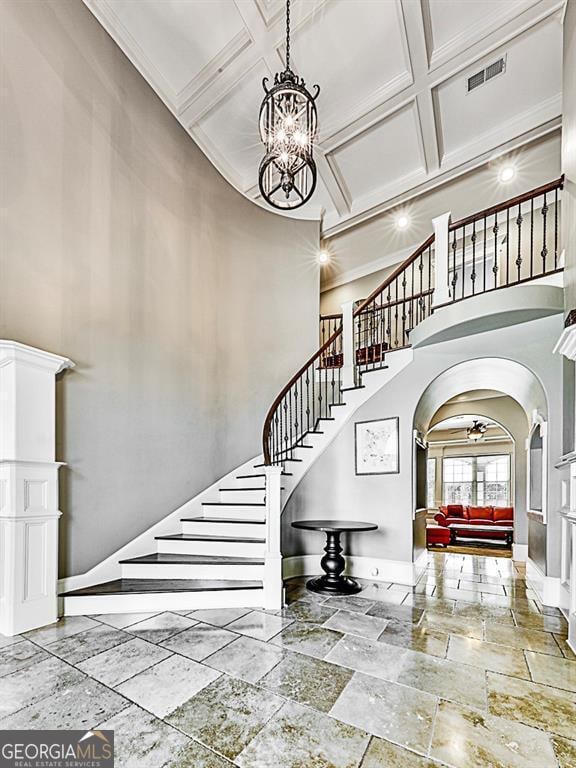 stairs with a notable chandelier, coffered ceiling, a towering ceiling, beam ceiling, and ornamental molding