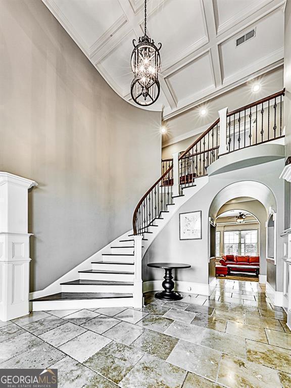 entrance foyer with arched walkways, coffered ceiling, a high ceiling, baseboards, and stairway