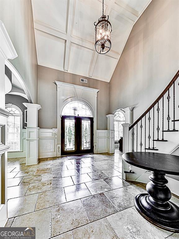 foyer with a decorative wall, high vaulted ceiling, stone tile flooring, arched walkways, and a chandelier