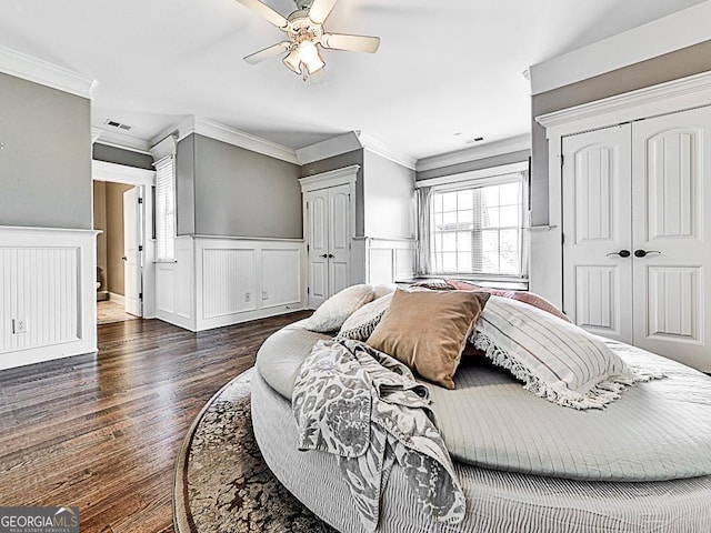 bedroom with dark wood-style flooring, crown molding, wainscoting, a ceiling fan, and a decorative wall