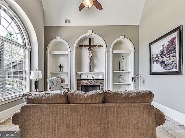 tiled living room featuring vaulted ceiling, built in features, ceiling fan, and a stone fireplace