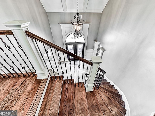 stairs with wood finished floors, a chandelier, and beam ceiling