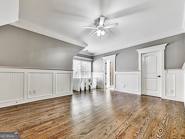 unfurnished living room with crown molding, a ceiling fan, a decorative wall, wood finished floors, and a wainscoted wall