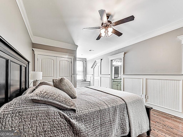 bedroom with ornamental molding, wood finished floors, a ceiling fan, and a wainscoted wall