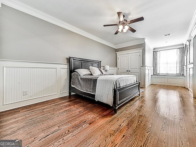 bedroom with wood finished floors, ornamental molding, a decorative wall, a wainscoted wall, and ceiling fan