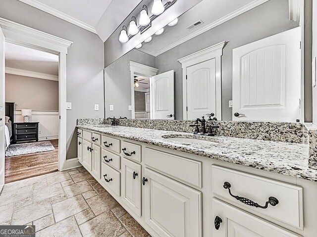 bathroom featuring crown molding, double vanity, stone tile flooring, ceiling fan, and baseboards