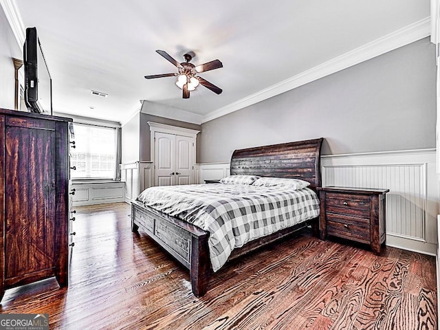bedroom with wood finished floors, wainscoting, ornamental molding, a ceiling fan, and a closet