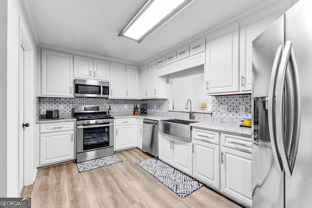 kitchen featuring light wood-type flooring, appliances with stainless steel finishes, backsplash, and white cabinets