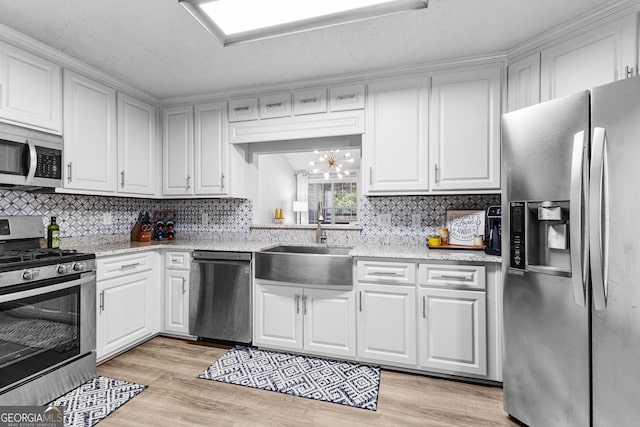 kitchen with an inviting chandelier, light hardwood / wood-style flooring, appliances with stainless steel finishes, sink, and light stone counters