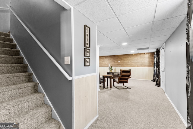 staircase featuring a paneled ceiling, carpet, and wooden walls