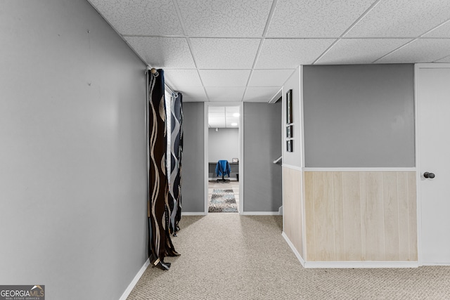 hall featuring a drop ceiling, wooden walls, and carpet floors