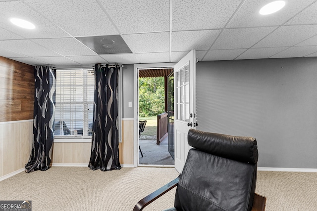 sitting room with carpet flooring, wooden walls, and a drop ceiling