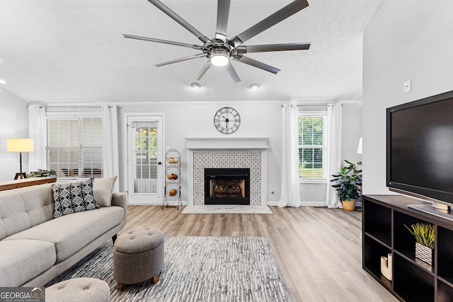 living room with ceiling fan, a fireplace, a textured ceiling, and light hardwood / wood-style flooring