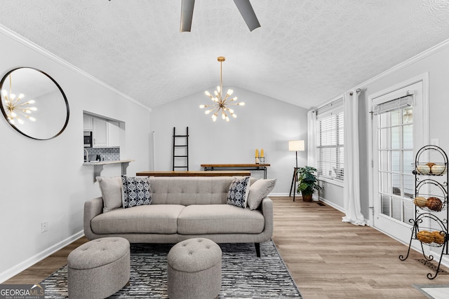 living room featuring a textured ceiling, ceiling fan with notable chandelier, light hardwood / wood-style floors, crown molding, and lofted ceiling