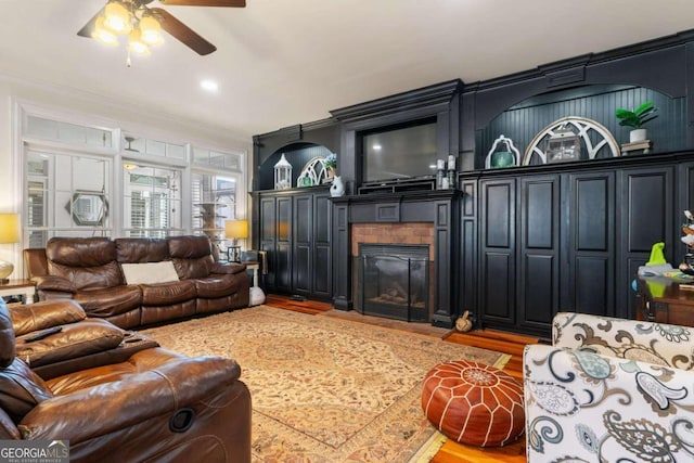 living room with ceiling fan, hardwood / wood-style flooring, crown molding, and a brick fireplace