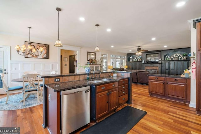 kitchen with ceiling fan with notable chandelier, dishwasher, light hardwood / wood-style floors, sink, and dark stone counters