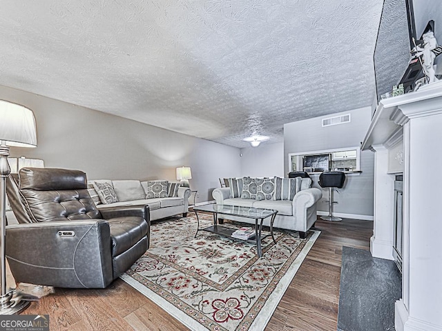 living room featuring visible vents, a textured ceiling, baseboards, and wood finished floors