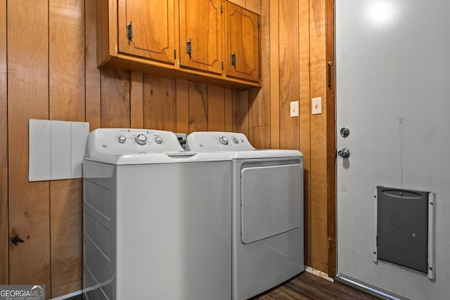 clothes washing area with dark wood-type flooring, cabinets, wooden walls, and separate washer and dryer