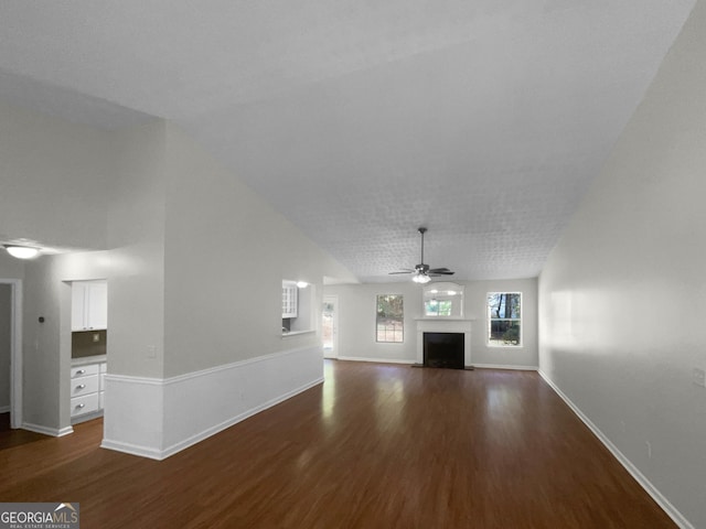 unfurnished living room featuring lofted ceiling, dark wood-type flooring, a fireplace with flush hearth, a ceiling fan, and baseboards