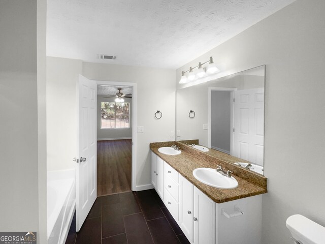 bathroom featuring hardwood / wood-style floors, a tub to relax in, vanity, ceiling fan, and a textured ceiling