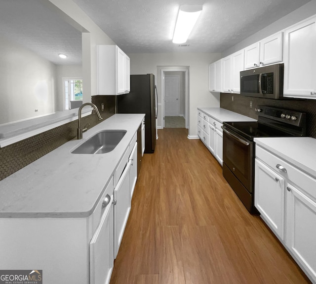 kitchen with black range with electric stovetop, wood finished floors, a sink, white cabinetry, and stainless steel microwave