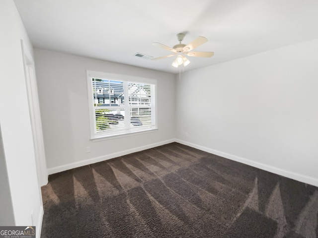 unfurnished room with a ceiling fan, visible vents, dark carpet, and baseboards