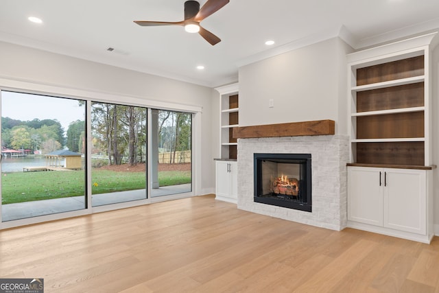 unfurnished living room with ceiling fan, a fireplace, crown molding, and light wood-type flooring