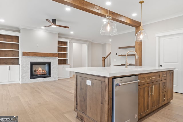 kitchen with sink, hanging light fixtures, a stone fireplace, light hardwood / wood-style flooring, and a center island with sink