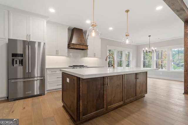 kitchen featuring custom range hood, light hardwood / wood-style flooring, stainless steel refrigerator with ice dispenser, and a center island with sink