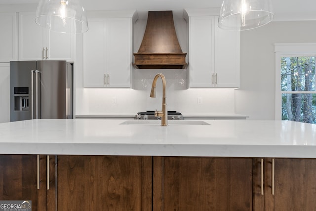 kitchen with white cabinetry, pendant lighting, high quality fridge, a center island with sink, and custom range hood