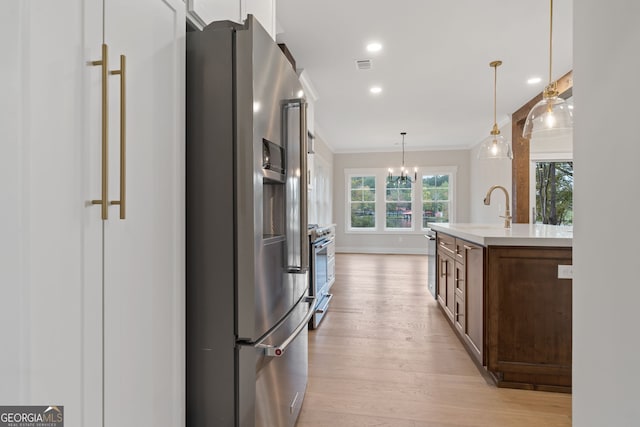 kitchen featuring appliances with stainless steel finishes, crown molding, sink, light hardwood / wood-style floors, and hanging light fixtures