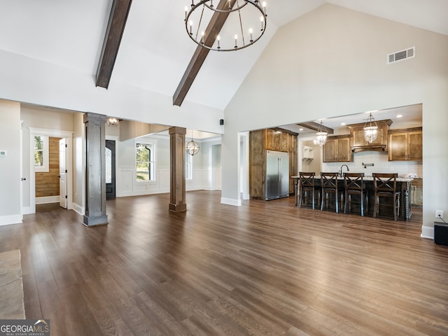 unfurnished living room featuring high vaulted ceiling, decorative columns, dark hardwood / wood-style flooring, an inviting chandelier, and beam ceiling