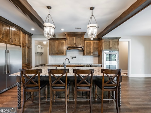 kitchen featuring appliances with stainless steel finishes, dark hardwood / wood-style floors, a kitchen island with sink, and a breakfast bar